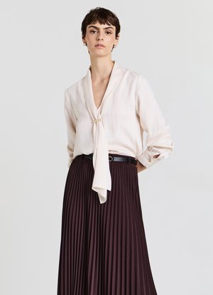 Light pink blouse with subtle vertical stripes and a tie at the neckline, paired with a long, pleated dark burgundy skirt and black belt.