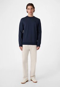 Granatowa, prążkowana bluza z dekoltem w kształcie litery V, z długimi rękawami i małym logo na piersi. Połączona z jasnobeżowymi spodniami i białymi tenisówkami.