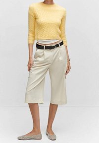 Keltainen neulottu lyhyt villapaita letin kuvioinnilla, yhdistetty beigen värisiin culottes-housuihin ja mustaan vyöhön. Kengät ovat vaaleanharmaat koristeilla.