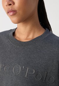 Felpa grigia con scollatura a costine, dal texture morbido e con un logo "Marc O'Polo" in rilievo ben visibile.