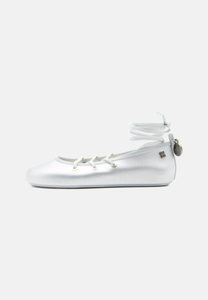 Balti baleto bateliai su kulkšnį apgaubiančia ryšio juosta, priekyje raišteliai ir mažas metalinis ženkliukas ant kulno dirželio, pateikti ant vientisos fono.