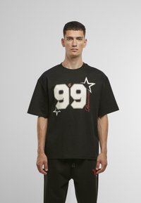 Musta puuvillapaita, jossa on suuri valkoinen "99" -design punaisilla yksityiskohdilla ja tähdellä. Rentomallinen ja lyhythihainen, yhdistettynä mustiin housuihin.