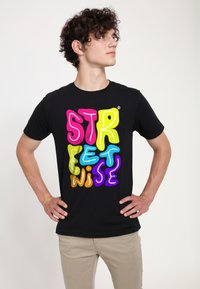 Černé bavlněné tričko s krátkým rukávem a kulatým výstřihem, zdobené barevným, nadýchaným textem "STREETWISE" v růžové, žluté, modré, oranžové a fialové barvě.