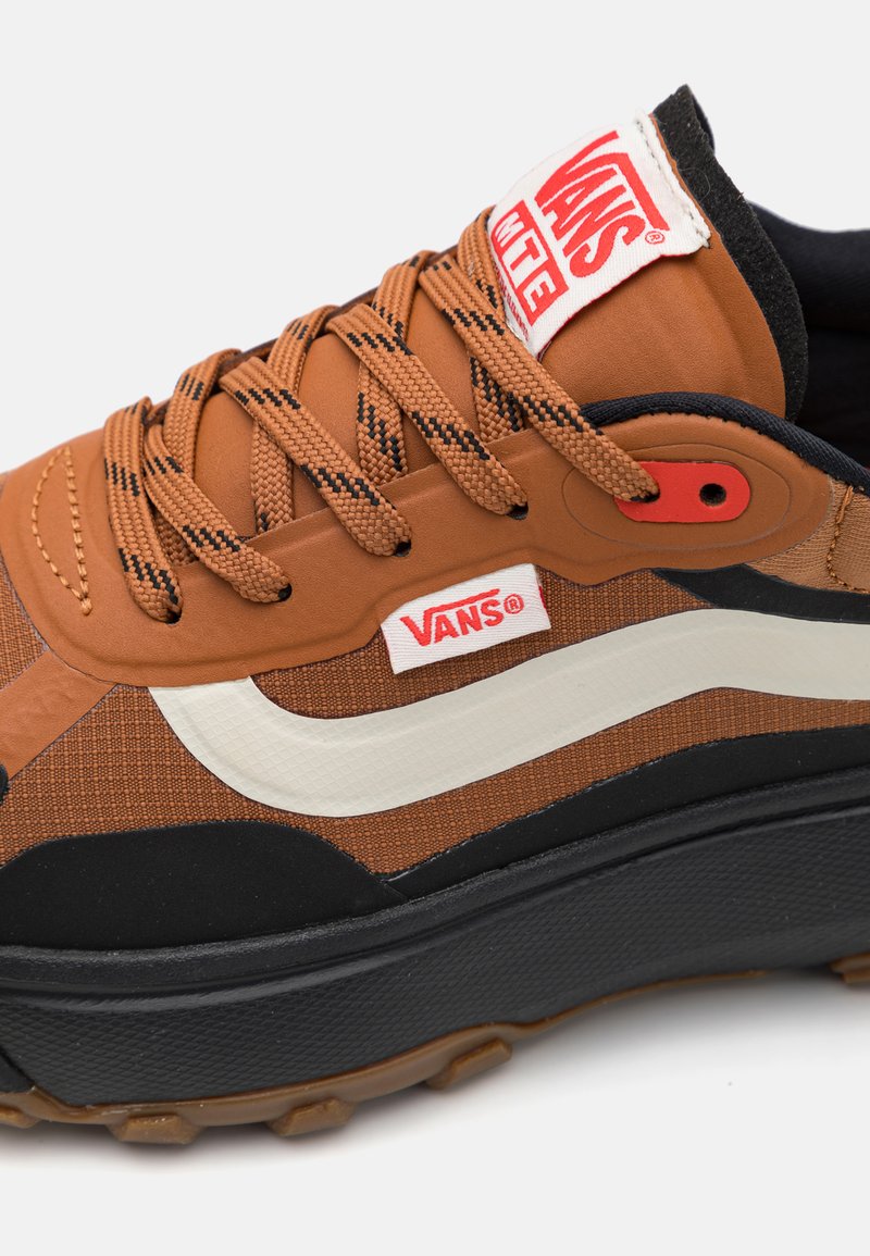 Sneaker Vans marrone con tomaia in tessuto testurizzato, accenti neri, striscia laterale bianca e suola in gomma spessa. Etichetta con logo rossa sulla linguetta.