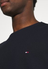 Marineblauer strukturierter Strickpullover mit Rundhalsausschnitt und kleinem rot-weißen-blauen Logo auf der Brust.