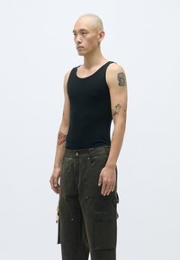 Μαύρο κ fitted αμάνικο μπλουζάκι με στρογγυλή λαιμόκοψη, σε συνδυασμό με ελαιόχρωμο cargo παντελόνι με πολλαπλές τσέπες και υφασμάτινη υφή.