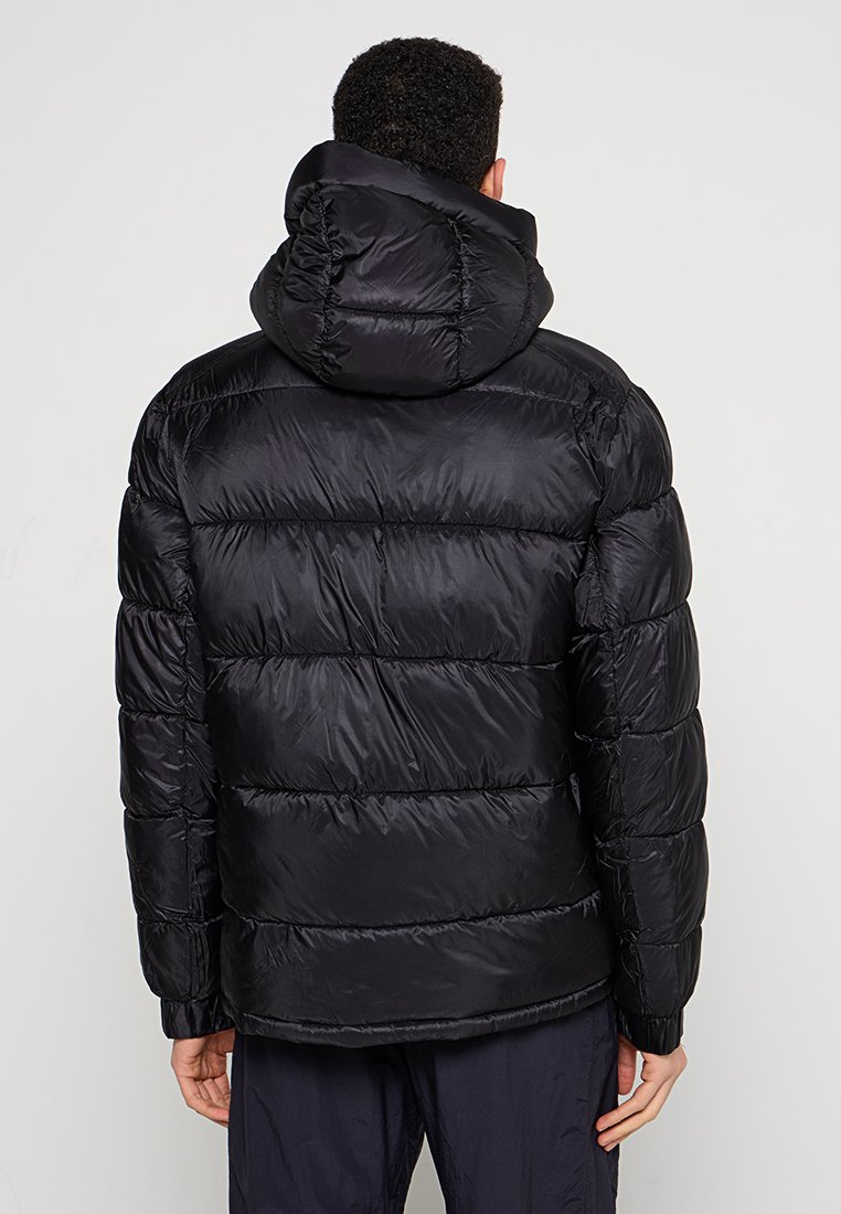 Giacca a vento nera con cappuccio, caratterizzata da un design trapuntato e una texture liscia. Il retro mostra un orlo leggermente accorciato e polsini elasticizzati.