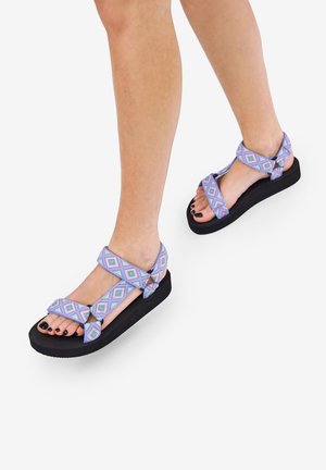 Sandalias moradas con un patrón y suelas negras gruesas. Las correas presentan un diseño de diamante en tonos de azul, rosa y lavanda, ofreciendo un ajuste seguro.