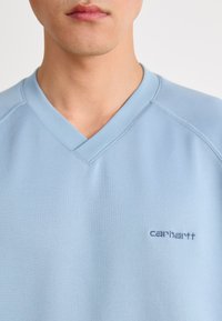 Light blue V-neck sweatshirt made of soft fabric. Features stitched collar and embroidered "Carhartt" logo on the chest.