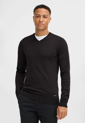 Svart v-ringad tröja med långa ärmar, figurnära design, ribbade manschetter och fåll, tillverkad av mjuk stickad tyg, bärs över en vit t-shirt.