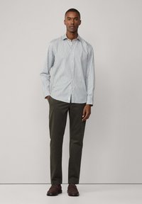 Heren overhemd met verticale blauwe en witte strepen, lange mouwen en een traditionele kraag, gecombineerd met olijfgroene broek.