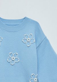 Suéter azul claro con cuello acanalado y bordado floral con acentos de perlas. Textura suave y corte relajado con mangas oversize.