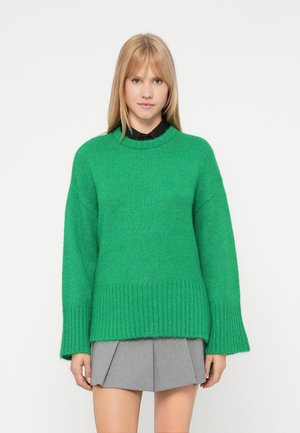 Roheline kudumisest särk ümmarguse kaeluse, soonikuvarrukate ja -äärtega. Lihtne, üle mõõdu suurusega disain, millele on juurde sobitatud hall volditud seelik.