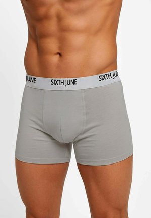 Boxer en coton gris avec une ceinture noire portant un logo, coupe ajustée et texture lisse. Sans motifs ni détails marquants.