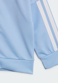 Hellblaues Sweatshirt aus strukturierter Baumwolle mit gerippten Bündchen und weißen Seitenstreifen. Weiches Material mit sportlichem, lässigem Design.