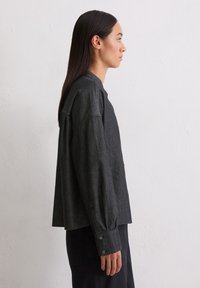 Camicia a maniche lunghe in denim nero con vestibilità rilassata, polsini con bottoni e design minimalista. La morbidezza del tessuto aumenta il comfort.