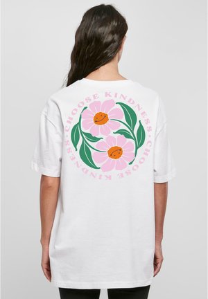Hvid t-shirt med et stort grafisk motiv på ryggen bestående af pink blomster, grønne blade og tekst, der lyder "Vælg venlighed" i pink og sort.