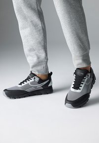 Schwarze und graue Sportschuhe mit Mesh- und Synthetiküberzügen, einer strukturierten Sohle und einer runden Zehenform. Akzente sind ein weißes Logo und Schnürsenkel.