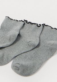 Γκρίζες κάλτσες με πλέγμα ριπ, που διαθέτουν ένα μαύρο ρυτιδωτό περίγραμμα γύρω από το επάνω μέρος. Το ύφασμα φαίνεται μαλακό και ευέλικτο.