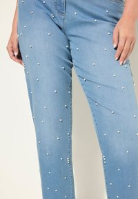 Ljust blå denimjeans prydda med vita pärlliknande detaljer, med en rak bendesign och en slät yta. Inga synliga fickor.