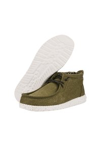 Botas hasta el tobillo de tela verde olivo con parte superior texturizada, cordones negros y suela blanca moteada. El interior cuenta con un forro estampado.