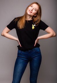 Black t-shirt with a banana graphic and text on the chest, paired with blue jeans. The model has long hair and is posing with hands on hips.