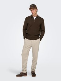 Brown zip-neck sweater, beige sweatpants, and dark brown shoes. The cap is brown with white logo. Simple, casual athletic outfit.