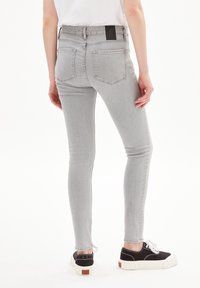 Jeans skinny de mezclilla gris con cintura alta, bolsillos traseros y un parche de marca en la cintura, combinados con zapatillas negras.