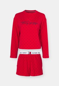 Röd pyjamasset bestående av en långärmad topp med marinblåa prickar och en "Tommy Hilfiger"-logotyp, i kombination med matchande röda shorts och en märkesresår.