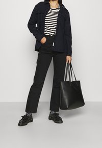 Musta takki, raidallinen paita, mustat housut ja mustat kengät, joissa on paksu pohja. Pitää isoa mustaa olkalaukkua. Yksinkertainen, moderni muotoilu.