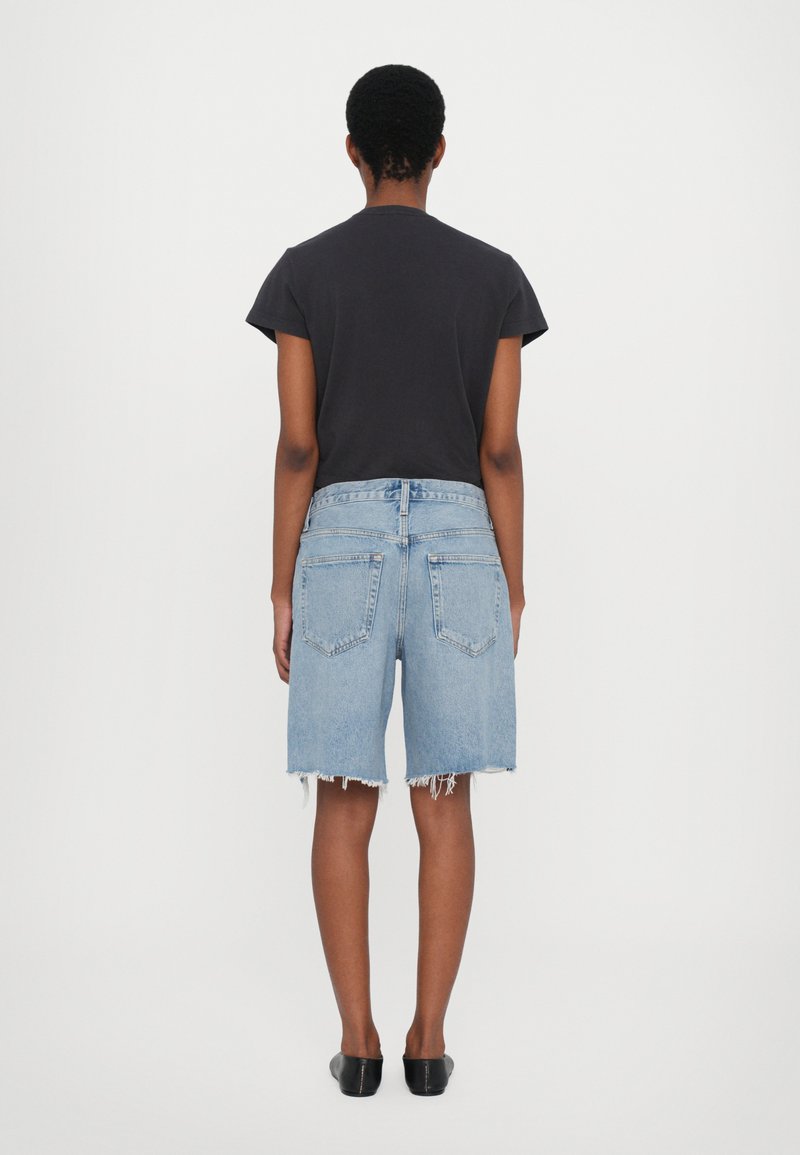 Denim shorts in light blue with frayed hem and five-pocket design, paired with a short-sleeve black T-shirt and black slip-on shoes.