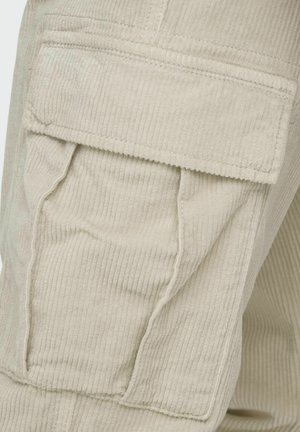 Beige corduroy fabric features a large patch pocket with a textured surface. The fabric has vertical ridges and visible stitching details.