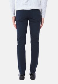 Pantaloni blu navy in cotone con design a gamba dritta, dotati di tasche posteriori e dettagli di cucitura sottili. Indossati con scarpe nere.