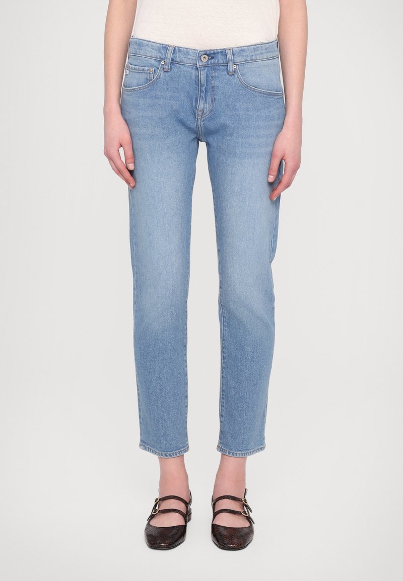 Jasnoniebieskie jeansy denimowe o prostym kroju nogawki, średnim stanie oraz pięciokieszeniowym wzorze, zestawione z ciemnymi, płaskimi butami.