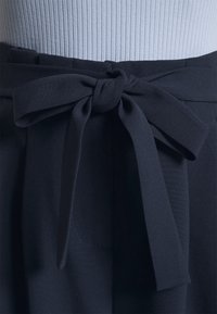 Navy blue fabric belt tied in a bow, with a smooth texture. The background is a light ribbed fabric, adding contrast to the dark belt.