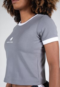 Grijze cropped t-shirt van rekbaar materiaal met witte kraag en mouwen, voorzien van een klein logo aan de voorkant.