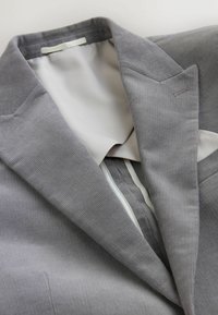 Grå kordflöjelblazer med utskurna slag, texturerad tyg och en mjuk vit foder. Har ren sömnad och skräddarsydd form.