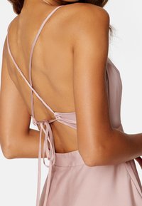 Robe rose pâle avec un dos décolleté, des bretelles fines croisées au dos et une fermeture à nouer pour un ajustement personnalisé. Texture de tissu lisse.