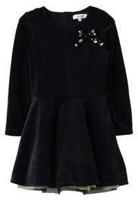 Black velvet dress with long sleeves, round neckline, flared skirt, and decorative bow with colorful gems on the left shoulder.