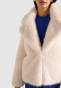 Faux fur jakke i blød pink, med en bred krave og en firkantet form. Teksturen er fluffy, med et rent, minimalistisk design.