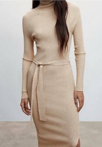 Vestito lavorato a maglia beige con texture a coste, collo alto, maniche lunghe e cintura in vita. La vestibilità è aderente e strutturata, con una lunghezza midi.