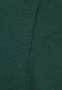 Närbild av texturerad mörkgrön tyg, som visar ett slätt och något ribbat mönster, vilket framhäver dess mjukhet och färgdjup.