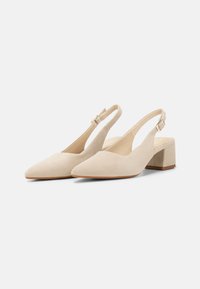 Beige semskede slingback-hæle med spids tå og en lav blokhæl. Har en sidelukning med spænde og en glat indvendig foring.