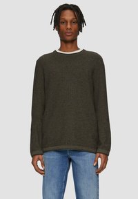 Dunkelgrüner Pullover mit langen Ärmeln, Rundhalsausschnitt und strukturiertem Stoff. Kombiniert mit hellblauen Jeans für einen lässigen Look.