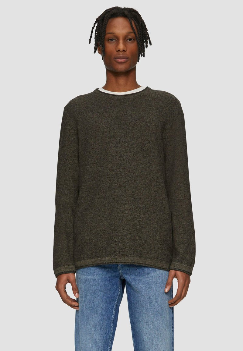 Dunkelgrüner Pullover mit langen Ärmeln, Rundhalsausschnitt und strukturiertem Stoff. Kombiniert mit hellblauen Jeans für einen lässigen Look.