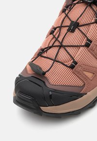 Rose mesh hiking shoe with black accents, featuring a textured rubber sole and elastic laces for adaptive fit. Durable design for outdoor use.