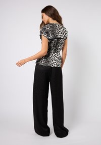 Leopardmønstret bluse med korte ermer, svarte detaljer og rynket bak, kombinert med svarte vidbukser med et subtilt mønster.