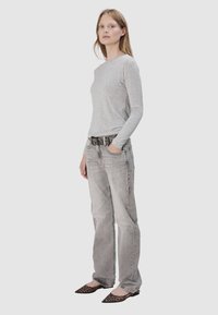 Szary długi rękaw, jasnoszare dżinsy, czarny i srebrny pasek oraz czarne płaskie buty w panterkę. Prosta, casualowa stylizacja, naturalna faktura materiału.