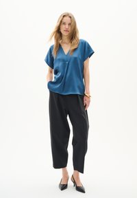 Top din satin albastru cu decolteu în V, mâneci scurte și față drapată, asortat cu pantaloni negri cu picioare largi și pantofi cu vârf ascuțit negri.