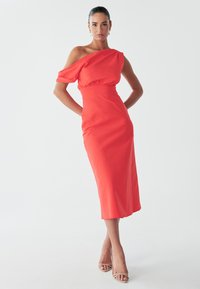 Punane ühe õlaga kleit, millel on liibuv ülaosa, vöökoht, mis on kokku tõmmatud, ja voolav seelik, valmistatud siledast kangast. Omadusena on pehme, drapeeritud varrukas.